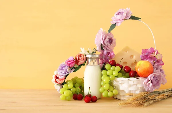 Imagem de frutas e queijo em cesta decorativa com flores sobre mesa de madeira. Símbolos de férias judaicas - Shavuot . — Fotografia de Stock