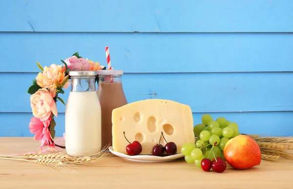 Bild av frukt och ost i dekorativ korg med blommor över träbord. Symboler för judiska semester - Shavuot. — Stockfoto