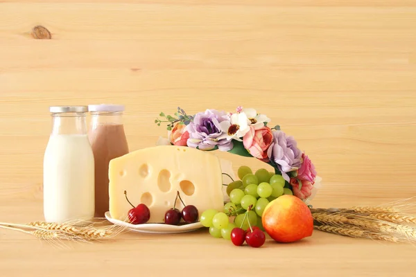 Bild von Früchten und Käse in dekorativem Korb mit Blumen über Holztisch. Symbole des jüdischen Feiertags - shavuot. — Stockfoto