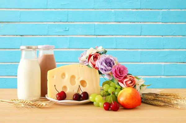 Изображение фруктов и сыра в декоративной корзине с цветами над деревянным столом. Символы еврейского праздника - Шавуот . — стоковое фото