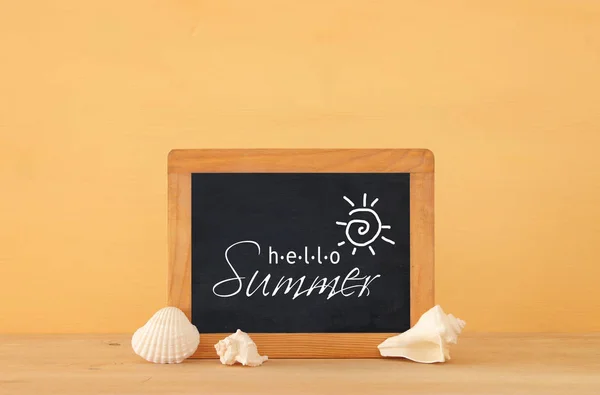 Nautical concept with blackboard and seashells over wooden table. — Stock Photo, Image