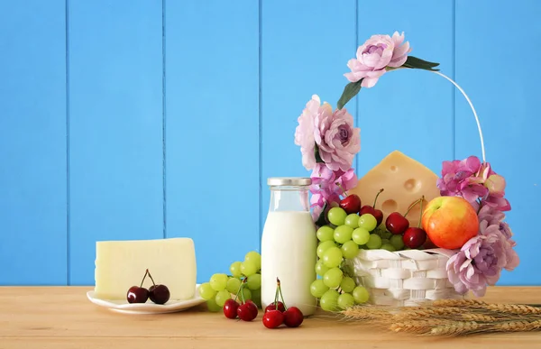 Bild von Früchten und Käse in dekorativem Korb mit Blumen über Holztisch. Symbole des jüdischen Feiertags - shavuot. — Stockfoto