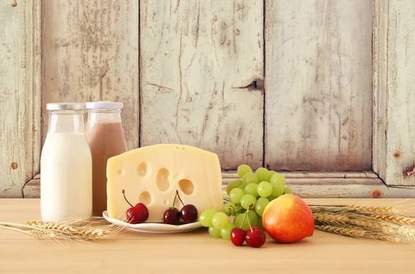 Bild von Früchten und Käse in dekorativem Korb mit Blumen über Holztisch. Symbole des jüdischen Feiertags - shavuot. — Stockfoto