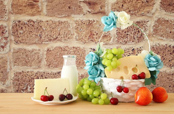 Imagen de frutas y queso en cesta decorativa con flores sobre mesa de madera. Símbolos de la fiesta judía - Shavuot . —  Fotos de Stock