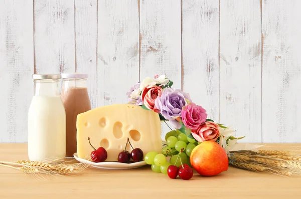 Bild von Früchten und Käse in dekorativem Korb mit Blumen über Holztisch. Symbole des jüdischen Feiertags - shavuot. — Stockfoto