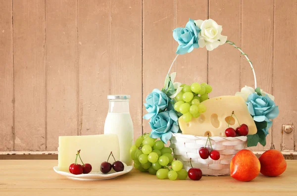 Imagem de frutas e queijo em cesta decorativa com flores sobre mesa de madeira. Símbolos de férias judaicas - Shavuot . — Fotografia de Stock