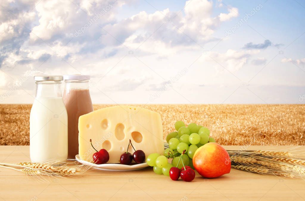 image of fruits and cheese in decorative basket with flowers over wooden table. Symbols of jewish holiday - Shavuot.