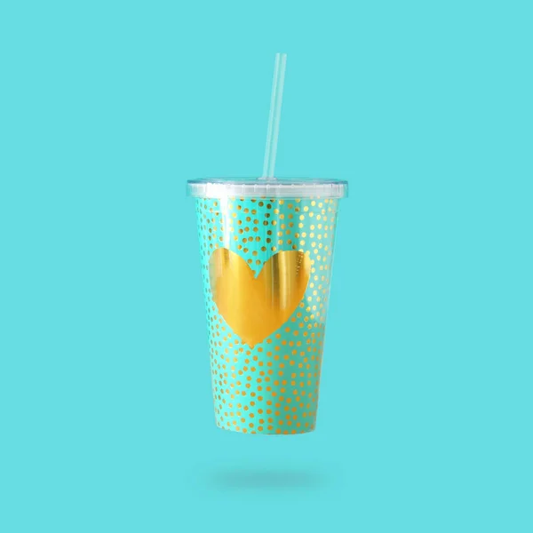 minimalism concept. mint plastic cup with gold heart decoration for soda or cold beverage with drinking straw.