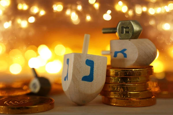 Religion concept of of jewish holiday Hanukkah with wooden dreidels (spinning top) and chocolate coins over wooden table and bokeh lights background — Stock Photo, Image