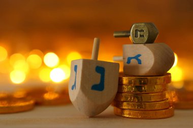 Dini bayram bayramı Hanuka kavramı ahşap topaç (dönen topaç) ve tahta masa üzerinde çikolata sikkeleri ve arka planda Bokeh ışıkları