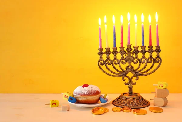 Náboženský obraz židovské dovolené Chanuka pozadí s menorah (tradiční svícen), točící se top, čokoládové mince a kobliha přes žluté pozadí — Stock fotografie