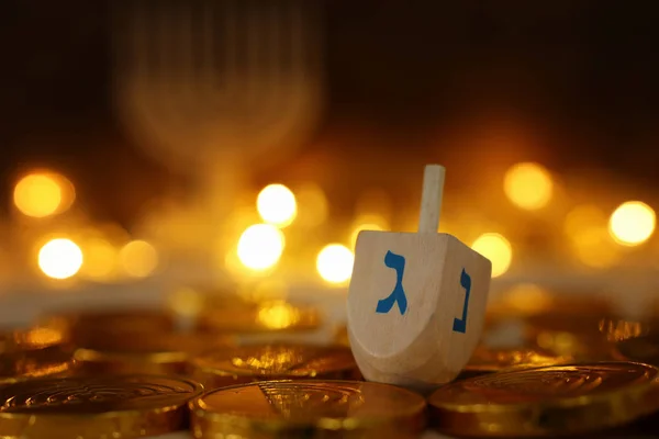 Религиозная концепция еврейского праздника Ханука с деревянными дрейделями (крутящийся верх) и шоколадными монетами на фоне деревянного стола и боке-огней — стоковое фото