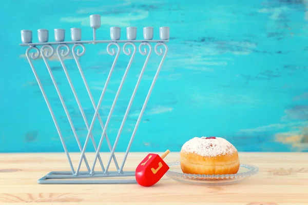 Imagen religiosa de fiesta judía Hanukkah con menorah (candelabro tradicional), peonza y rosquilla sobre mesa de madera y fondo azul —  Fotos de Stock