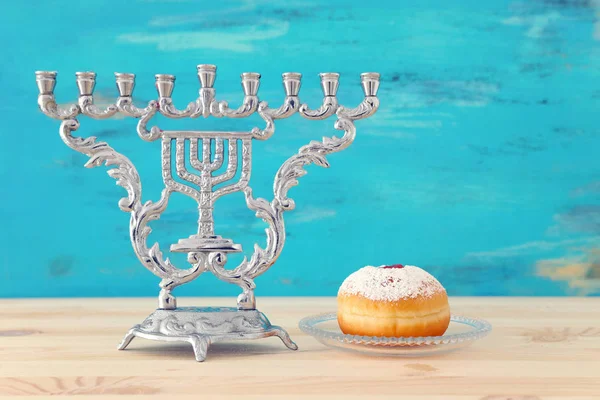 Religion image of jewish holiday Hanukkah with menorah (traditional candelabra) doughnut over wooden table and blue background — 图库照片