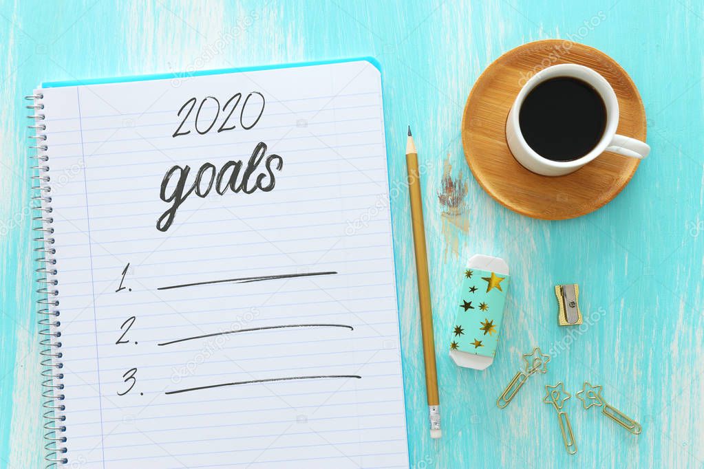 Business concept of top view 2020 goals list with notebook, cup of coffee over blue wooden desk