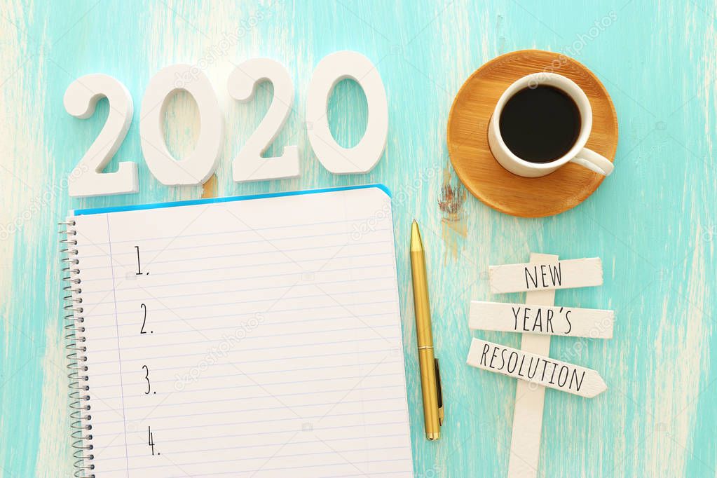 Business concept of top view 2020 goals list with notebook, cup of coffee over blue wooden desk