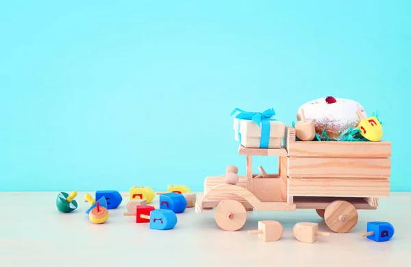 Религиозный образ еврейского праздника Ханука с крутящимся верхом и пончиком на деревянном автомобиле игрушка и пастельно-голубой фон — стоковое фото