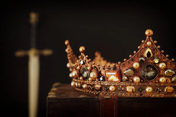 Imagen de llave baja de la hermosa corona reina / rey sobre la caja antigua junto a la espada. época medieval de fantasía. Enfoque selectivo — Foto de Stock