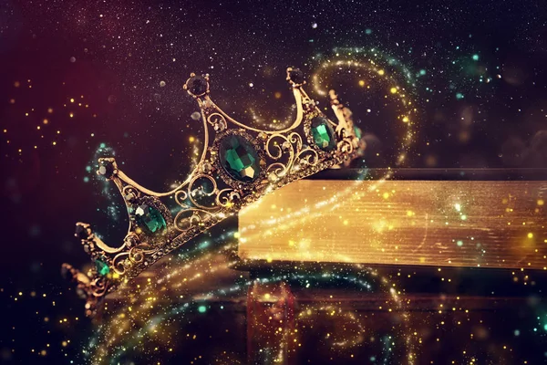 Imagen de llave baja de hermosa corona reina / rey sobre libro viejo y mesa de madera. filtrado vintage. época medieval de fantasía. Luces de brillo — Foto de Stock