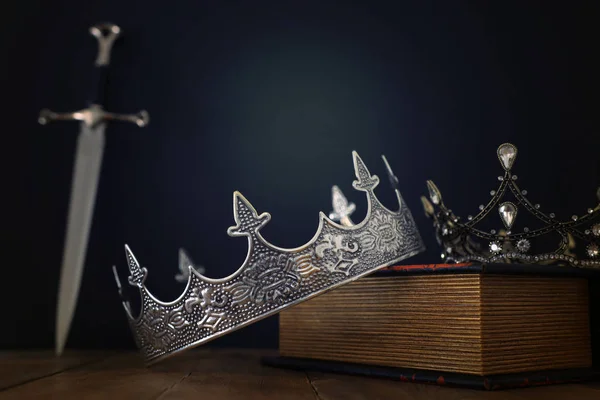 Низкий ключевой образ красивой королевы / короля корону над антикварной книги рядом с мечом. Средневековый период фантазий. Селективный фокус — стоковое фото