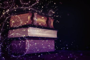 Eski ahşap masanın üzerinde bir yığın antika kitap. fantezi ortaçağ dönemi ve dini kavram. Parıldayan ışıklar.