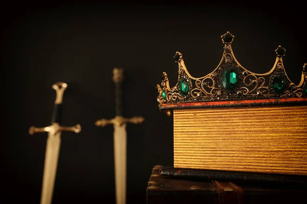 剣の横にあるアンティーク本の上に美しい女王/王の王冠の低キーイメージ。ファンタジー中世。選択的焦点 — ストック写真