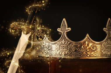 Kılıcın yanındaki antika kutunun üzerinde güzel kraliçe ve kral tacının gösterişsiz görüntüsü. fantezi ortaçağ dönemi. Seçici odaklanma. Parıldayan ışıklar.