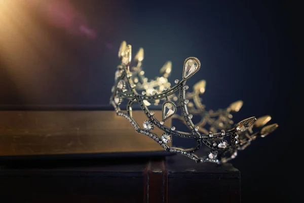 Laag sleutelbeeld van mooie koningin / koningskroon over oud boek en houten tafel. vintage gefilterd. fantasie middeleeuwse periode — Stockfoto