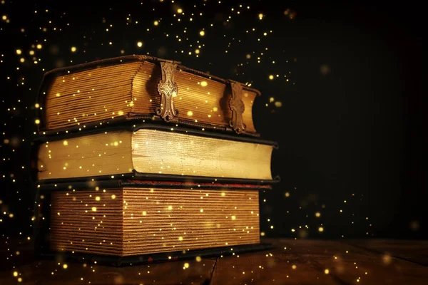 Pila de libros antiguos en la vieja mesa de madera. fantasía medieval y concepto religioso. Luces de brillo —  Fotos de Stock
