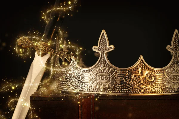 Lage sleutel beeld van mooie koningin / koning kroon over antieke doos naast zwaard. fantasie middeleeuwse periode. Selectieve focus. Glitter fonkelende lichten — Stockfoto
