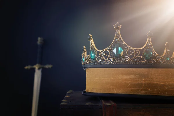 Low key image of beautiful queen/king crown over antique book next to sword. fantasy medieval period. Selective focus — Stock Photo, Image