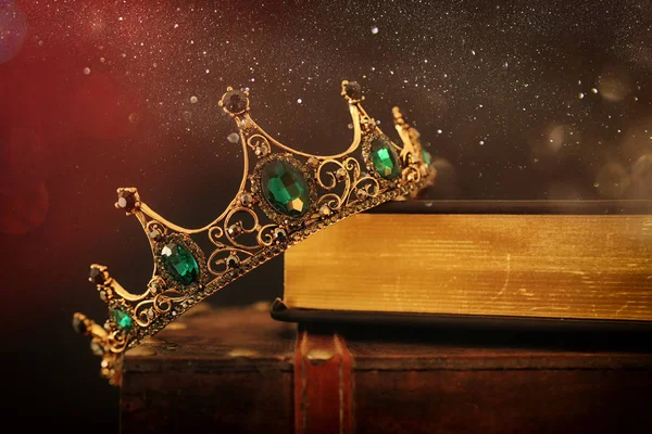 Niski kluczowy obraz pięknej królowej / korony króla nad starą książką i drewnianym stołem. vintage filtrowane. okres średniowiecza fantasy — Zdjęcie stockowe