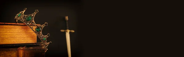 Imagen de llave baja de hermosa corona reina / rey sobre libro antiguo al lado de la espada. época medieval de fantasía. Enfoque selectivo —  Fotos de Stock