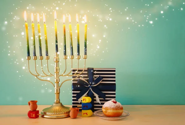 Náboženský obraz židovské dovolené Chanuka s menorah (tradiční svícen), točící se vrchol a kobliha přes dřevěné pozadí — Stock fotografie
