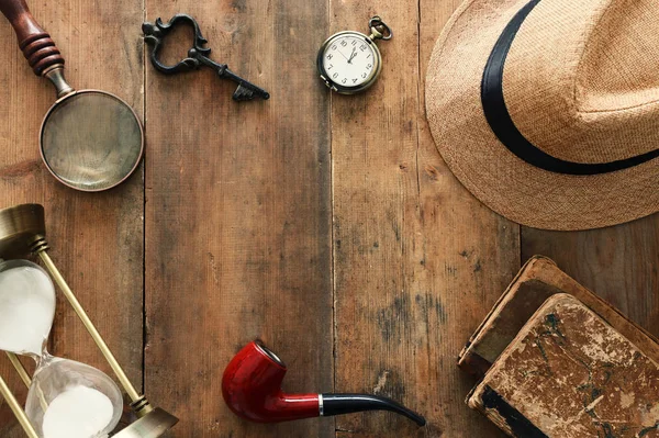 Concept image of investigation or private detective. Fedora hat, magnifing glass and vintage items over wooden table