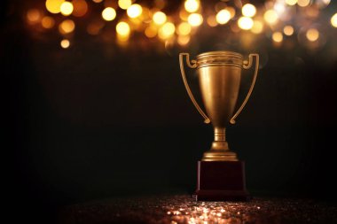 düşük anahtar görüntü Trophy üzerinde ahşap masa ve soyut parlak ışıklar ile koyu arka plan