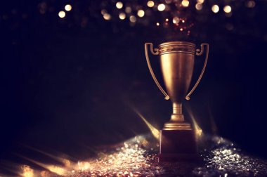 düşük anahtar görüntü Trophy üzerinde ahşap masa ve soyut parlak ışıklar ile koyu arka plan