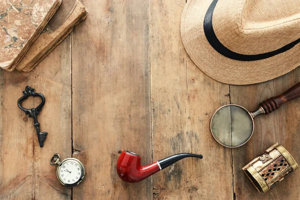 Concept image of investigation or private detective. Fedora hat, magnifying glass and vintage items over wooden table — Stock Photo, Image