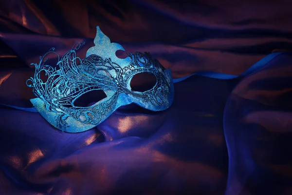 Foto de máscara veneziana azul elegante e delicado sobre fundo de seda roxo — Fotografia de Stock