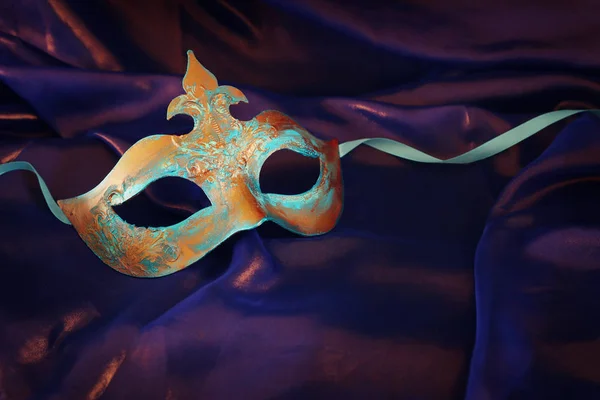 Foto de elegante e delicado azul e bronze máscara veneziana sobre fundo de seda roxo — Fotografia de Stock