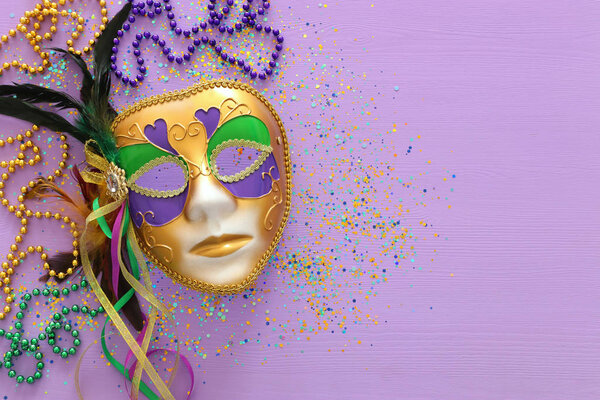 Holidays image of mardi gras masquarade, venetian mask and beads over purple background. view from above