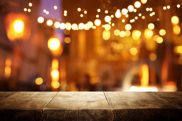 Изображение деревянного стола перед размытыми огнями ресторана