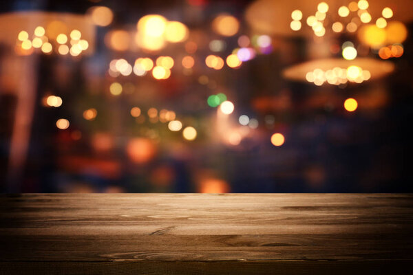 Изображение деревянного стола перед размытыми огнями ресторана