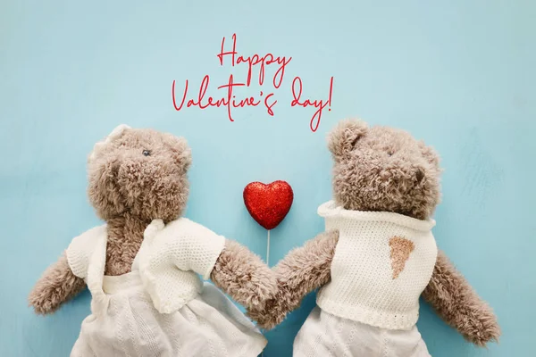 Концепція Дня Святого Валентина. Пара милих плюшевих ведмедів тримає серце над синім дерев'яним тлом — стокове фото