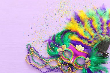 Mardi Gras maskesi, Venedik maskesi ve mor arka planda yelpaze tatili görüntüsü. Yukarıdan görünüm