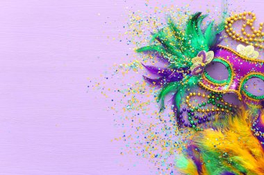 Mardi Gras maskesi, Venedik maskesi ve mor arka planda yelpaze tatili görüntüsü. Yukarıdan görünüm