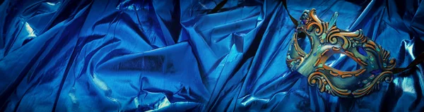 Foto de máscara veneziana elegante e delicada sobre fundo de seda azul — Fotografia de Stock