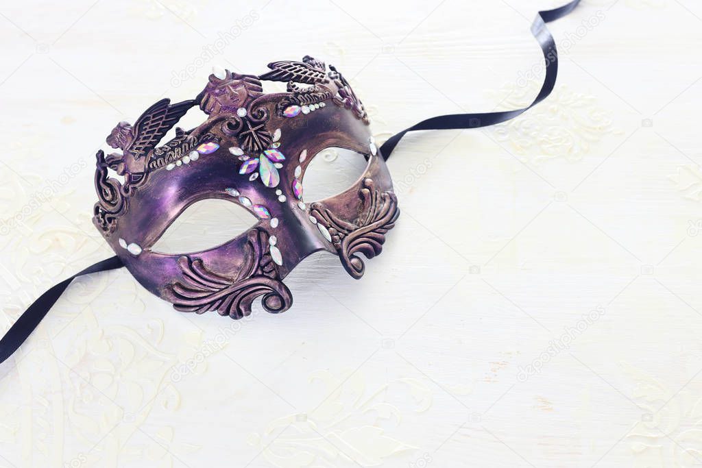 Photo of elegant and delicate purple Venetian mask over white wooden background