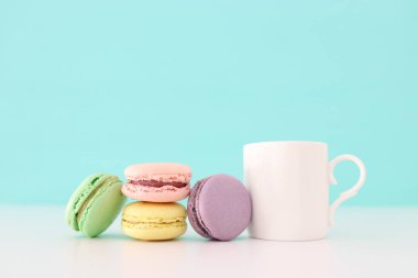 Beyaz kahve ve renkli badem kurabiyesi ya da pastel ahşap masanın üzerinde badem kurabiyesi.