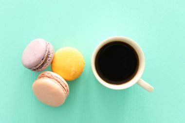 Beyaz kahve ve renkli badem kurabiyesi ya da pastel ahşap masanın üzerinde badem kurabiyesi.